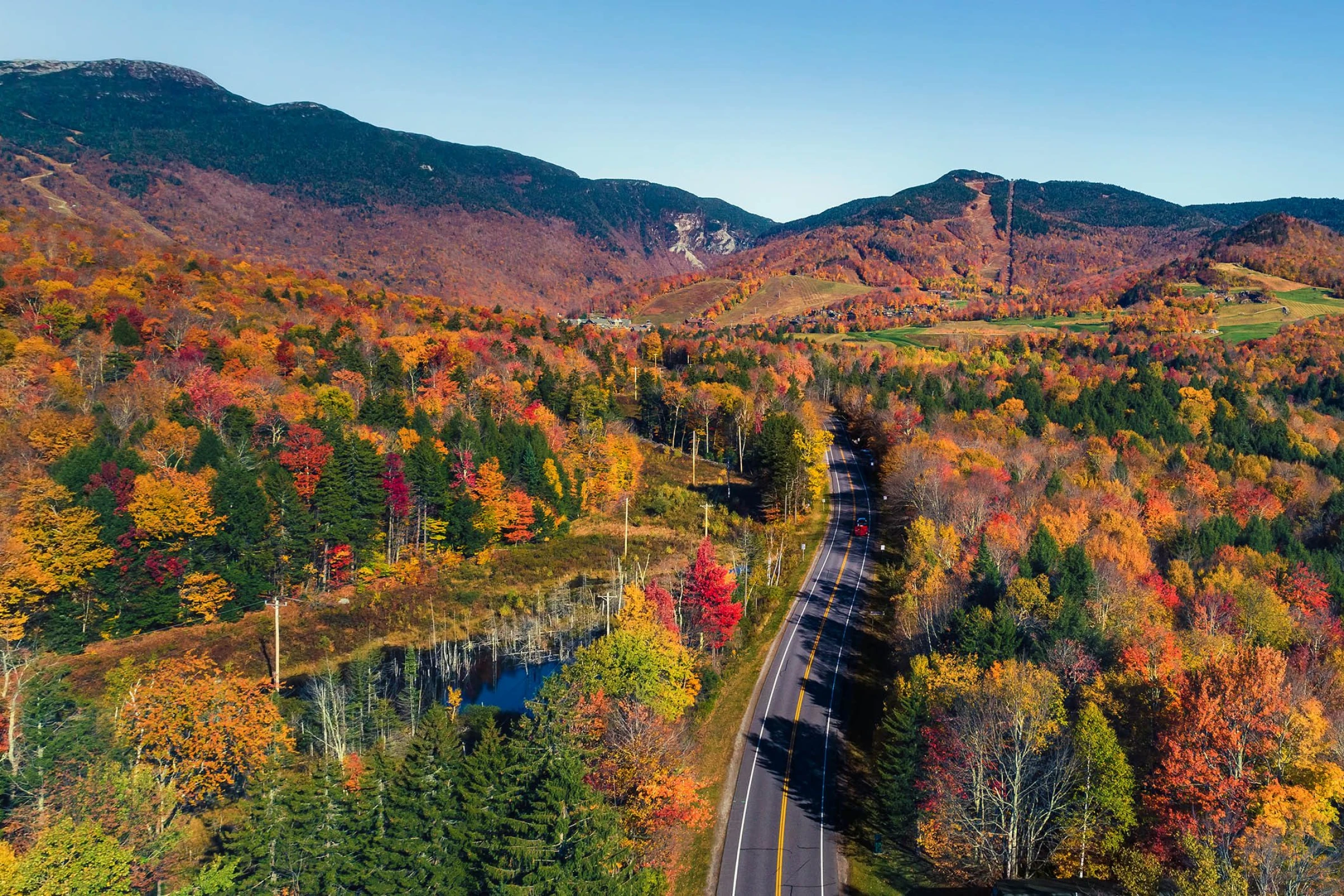 An overhead shot of a paved road in Stowe Vermont surrounded by foliage and mountains.