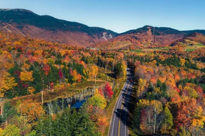 An overhead shot of a paved road in Stowe Vermont surrounded by foliage and mountains.